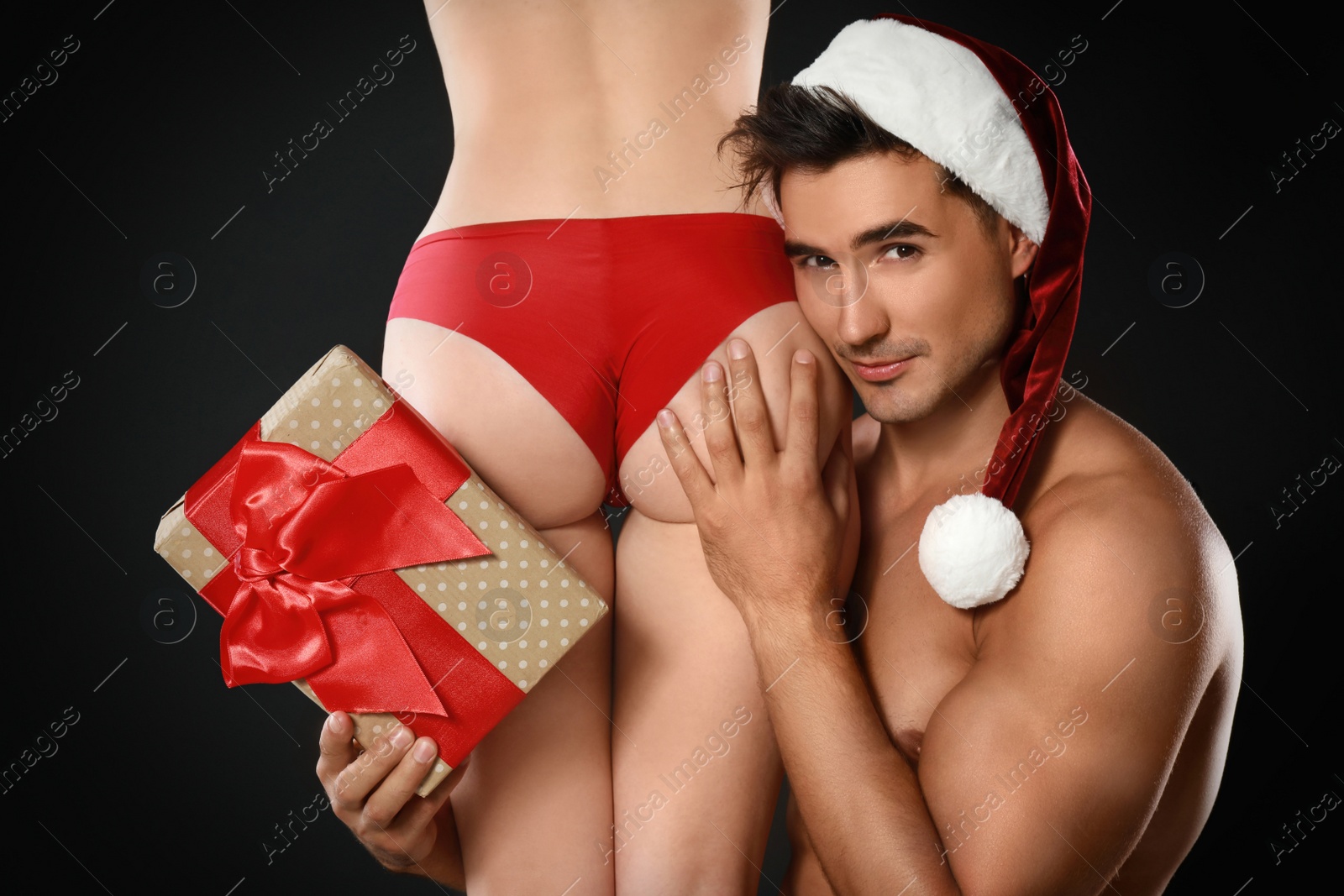 Photo of Attractive young Santa Claus with sexy woman and gift on dark background