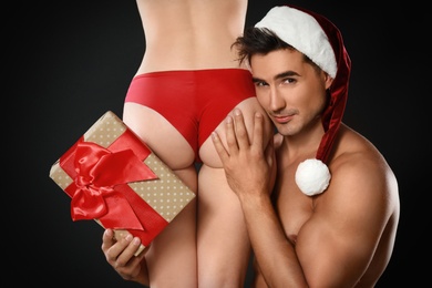 Attractive young Santa Claus with sexy woman and gift on dark background