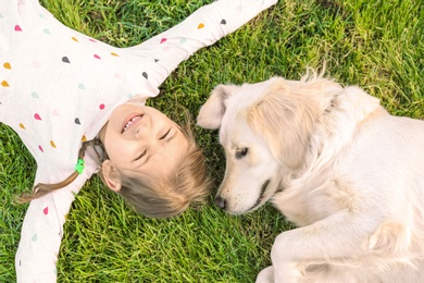 Photo of Cute little child with his pet on green grass, top view