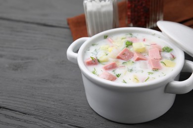 Delicious cold summer soup (okroshka) with boiled sausage in pot on grey wooden table, space for text