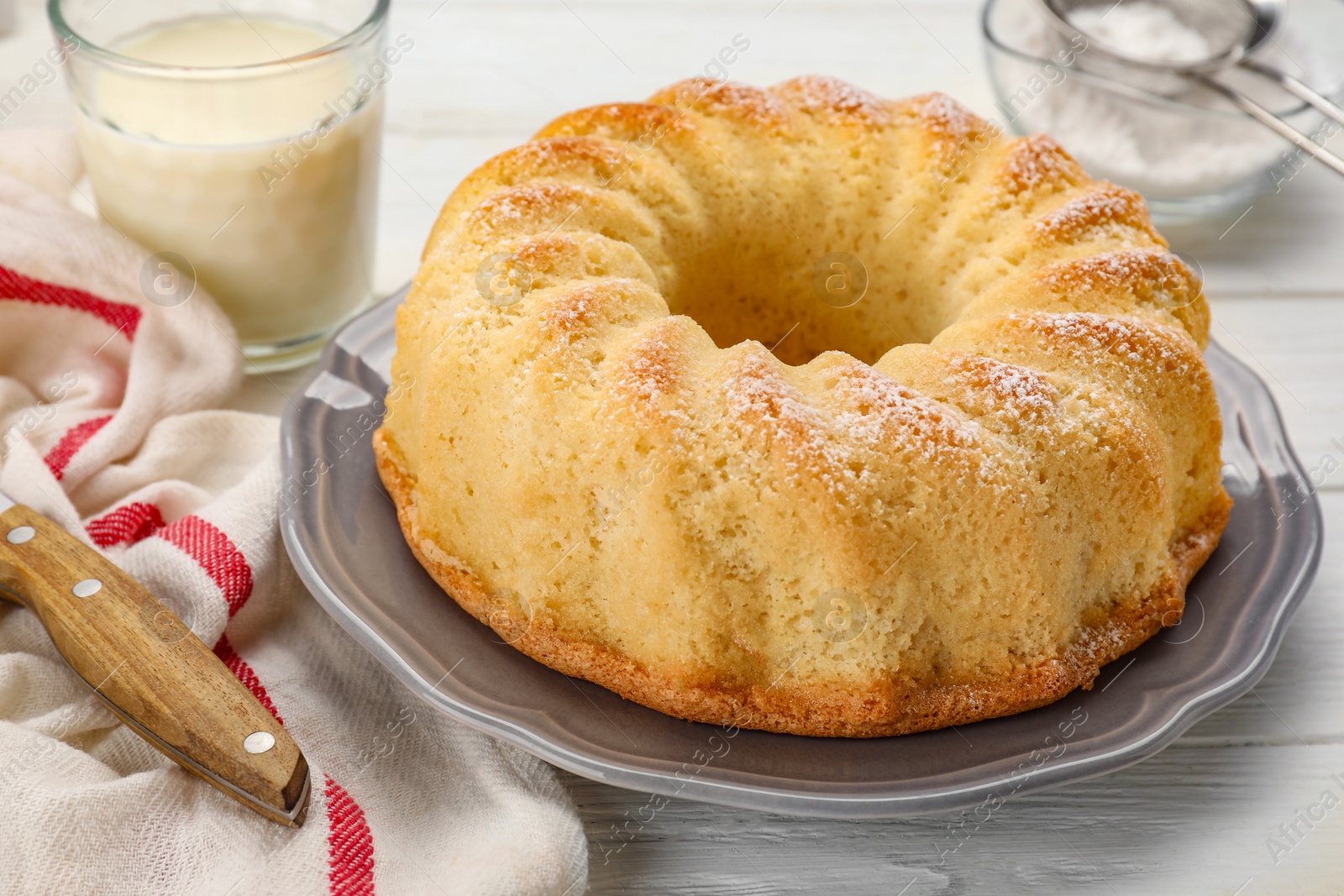 Photo of Delicious freshly baked sponge cake with powdered sugar and glass of milk on table, closeup