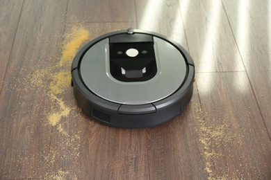 Modern robotic vacuum cleaner removing scattered groats from wooden floor
