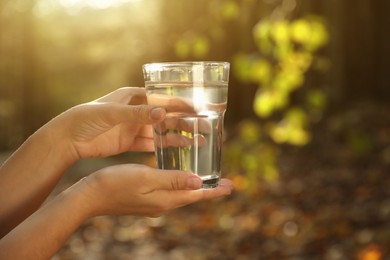 Photo of Woman holding glass of fresh water in forest, closeup