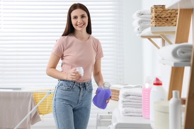 Photo of Woman holding fabric softener near washing machine in bathroom