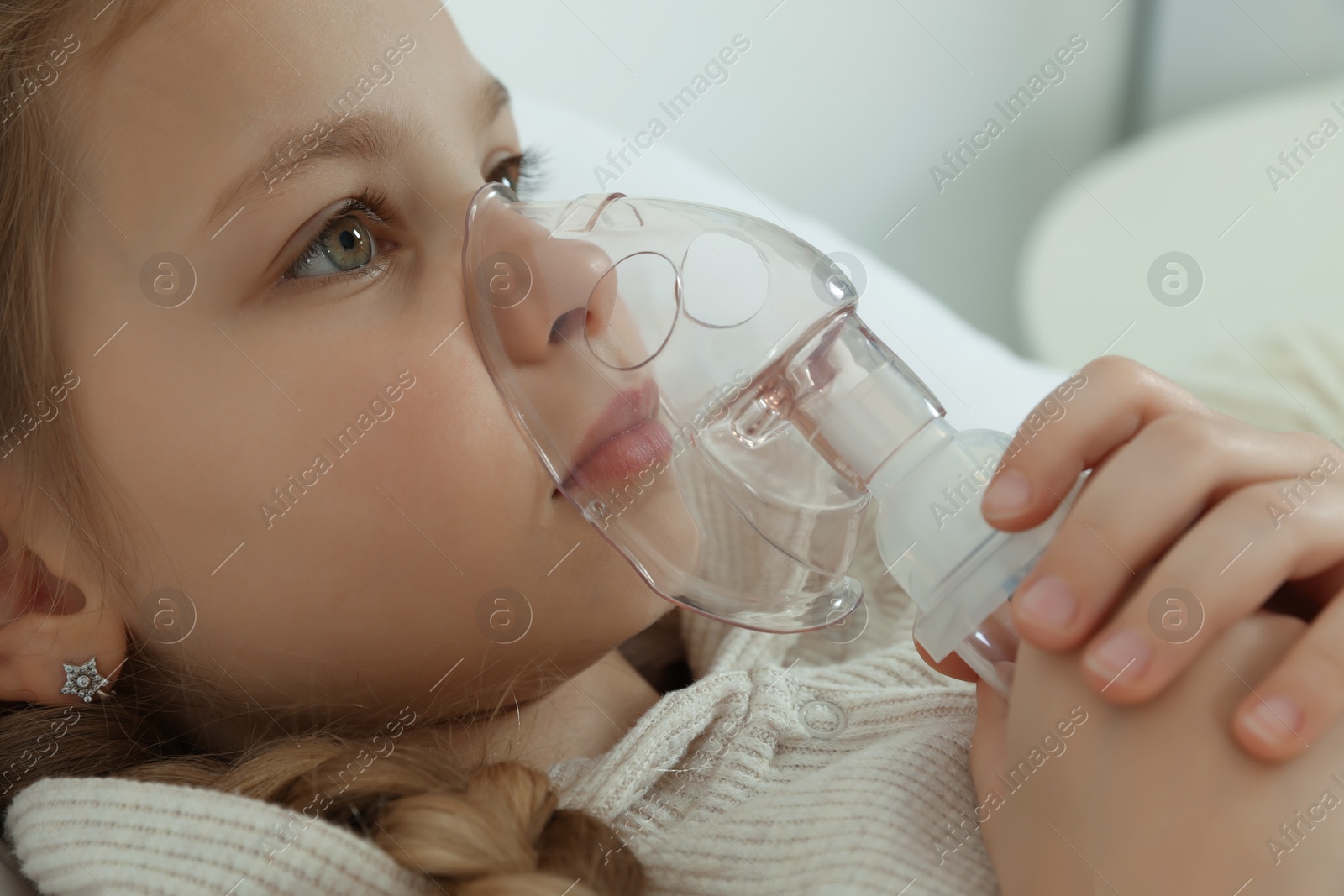 Photo of Little girl using nebulizer for inhalation indoors, closeup