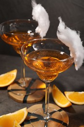 Photo of Tasty cocktails in glasses decorated with cotton candy and orange slices on gray table, closeup
