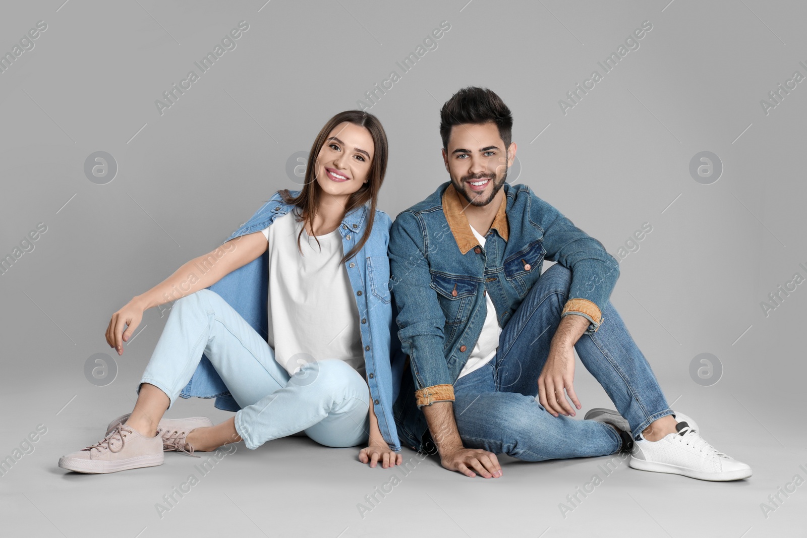 Photo of Young couple in stylish jeans sitting on grey background