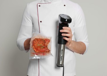Chef holding sous vide cooker and meat in vacuum pack on beige background, closeup