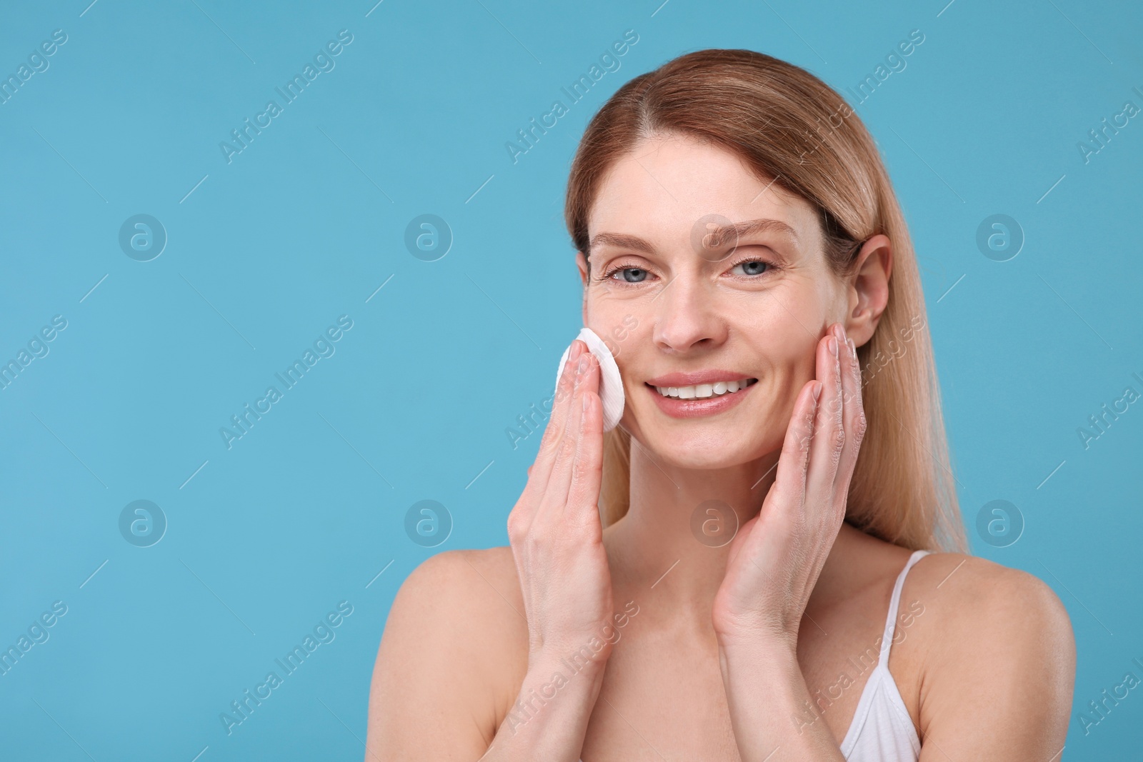 Photo of Beautiful woman removing makeup with cotton pad on light blue background, space for text