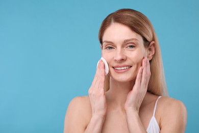 Beautiful woman removing makeup with cotton pad on light blue background, space for text