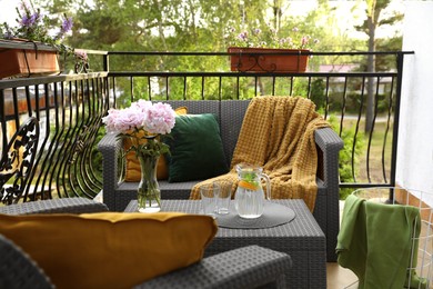 Photo of Rattan table with jug of water, glasses and beautiful flowers on terrace