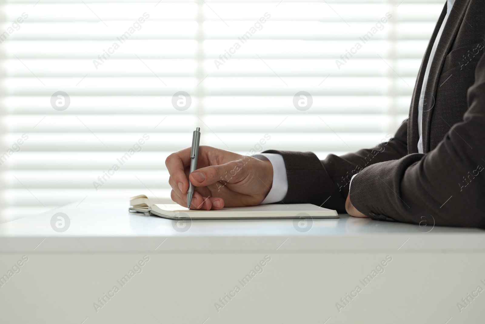 Photo of Man writing in notebook at white table, closeup