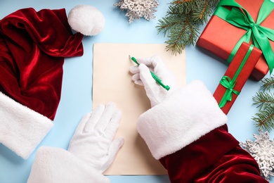 Top view of Santa writing letter at light blue table, closeup