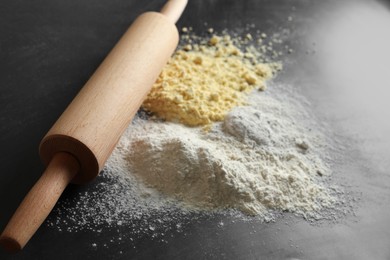 Rolling pin and different types of flour on black table, closeup