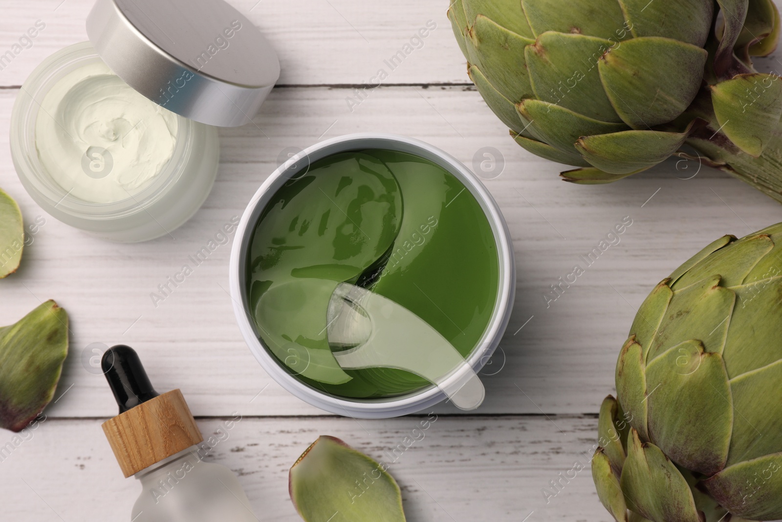 Photo of Package of under eye patches, cosmetic products and artichokes on white wooden table, flat lay