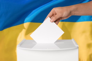 Image of Man putting his vote into ballot box against national flag of Ukraine, closeup