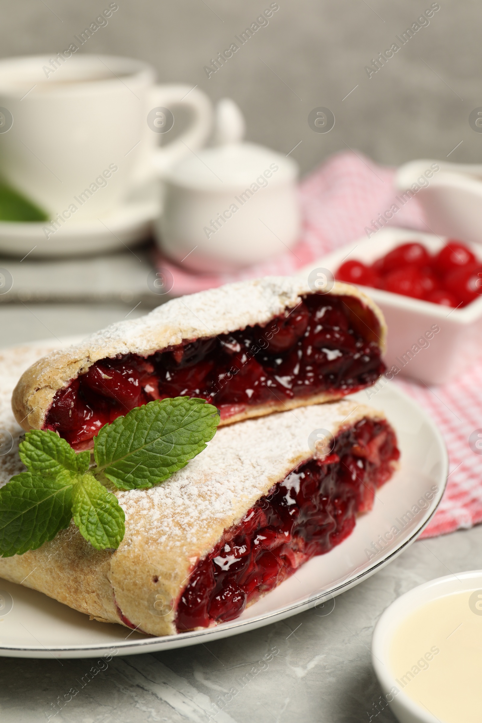 Photo of Delicious strudel with cherries, powdered sugar and mint on grey table, closeup