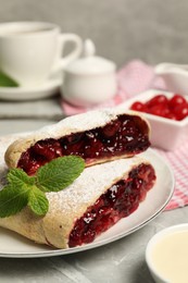 Delicious strudel with cherries, powdered sugar and mint on grey table, closeup