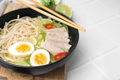 Photo of Bowl of delicious rice noodle soup with meat and egg on white tiled table, closeup. Space for text