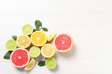 Different cut citrus fruits and leaves on white wooden table, flat lay. Space for text