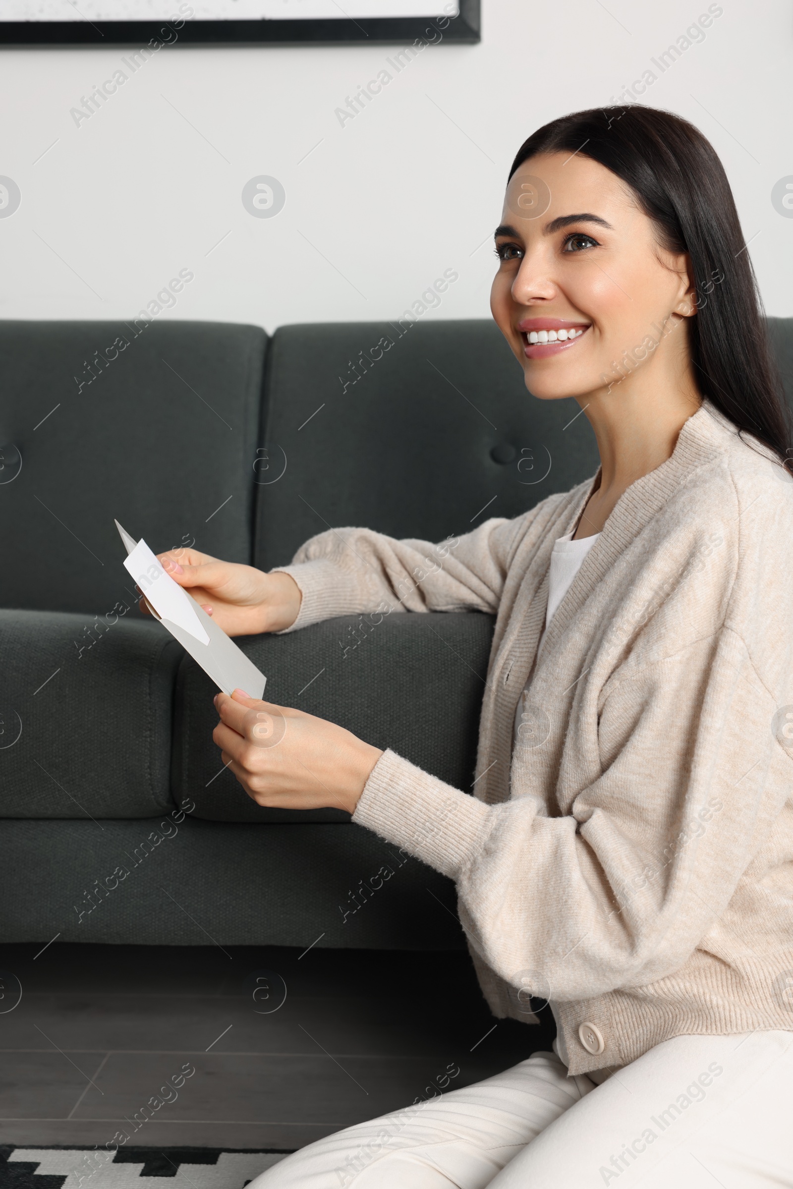 Photo of Happy woman reading greeting card on floor in living room