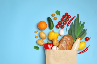 Shopping paper bag with different groceries on light blue background, flat lay. Space for text