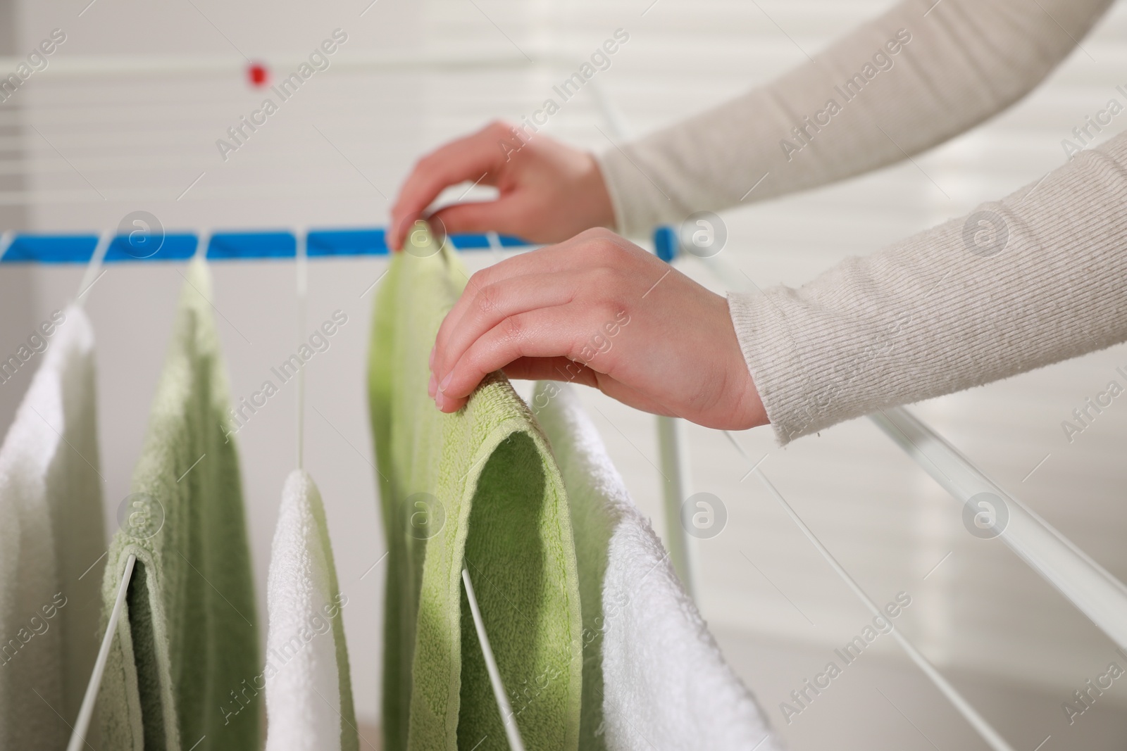 Photo of Woman hanging clean terry towels on drying rack indoors, closeup