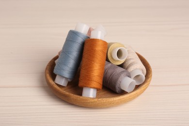 Photo of Bowl with color sewing threads on wooden table