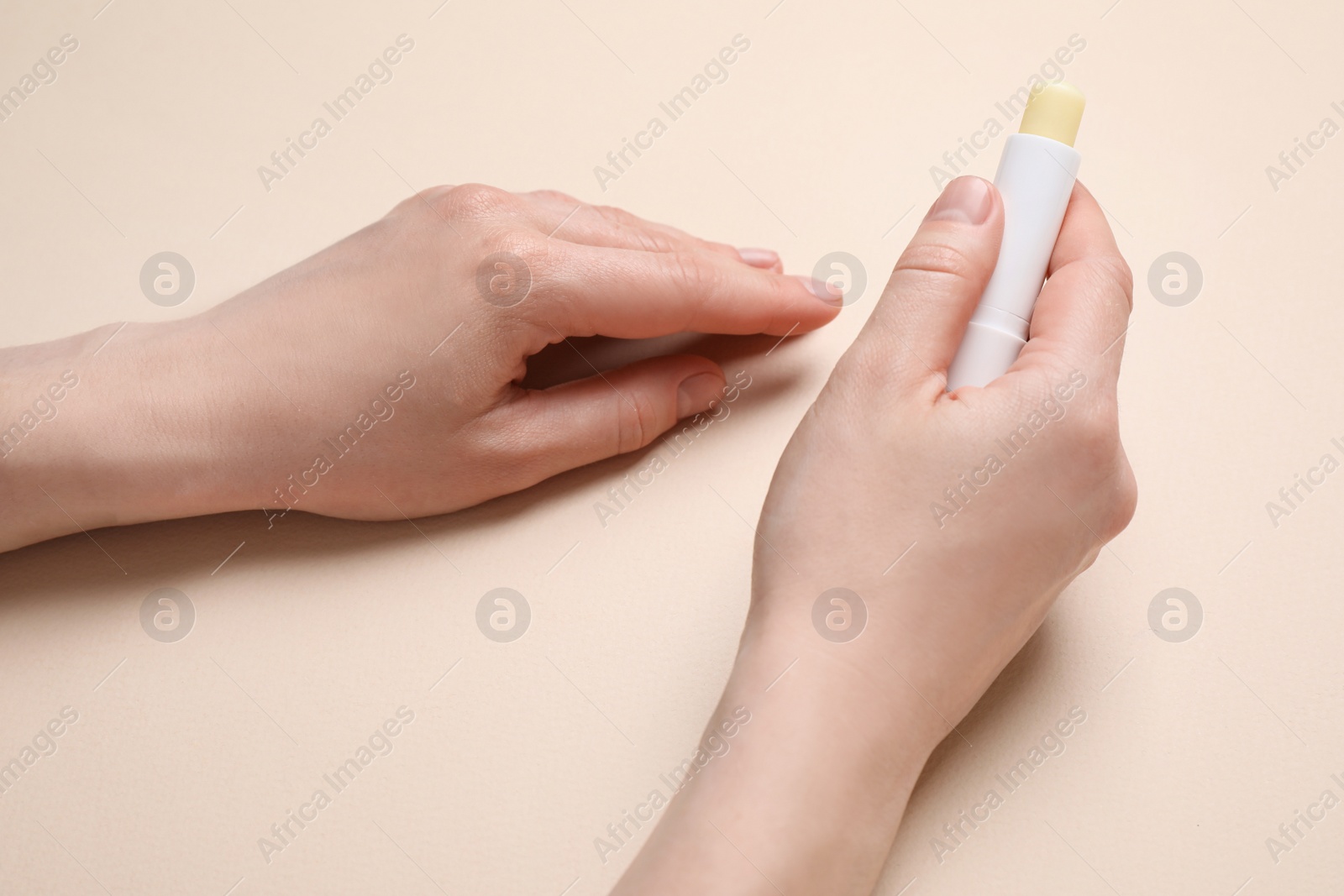 Photo of Woman holding hygienic lipstick on beige background, closeup