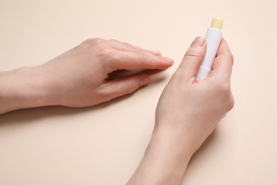 Photo of Woman holding hygienic lipstick on beige background, closeup