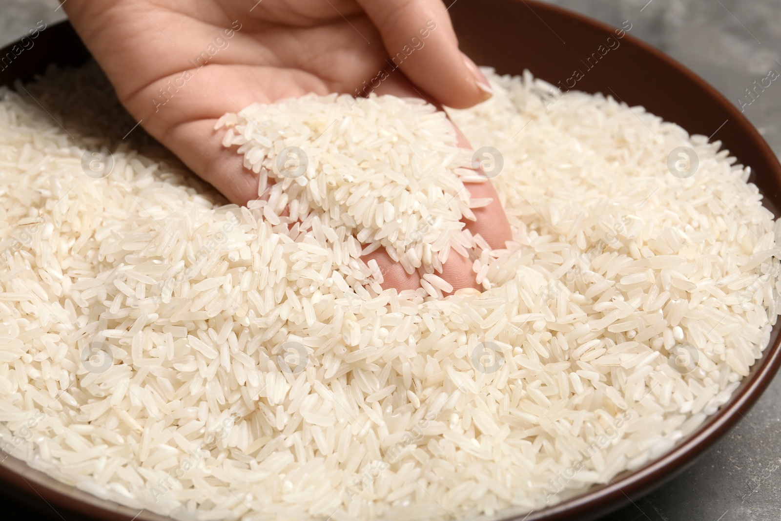 Photo of Woman holding grains near plate with rice on table, closeup