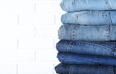 Photo of Stack of different jeans near white brick wall, closeup. Space for text