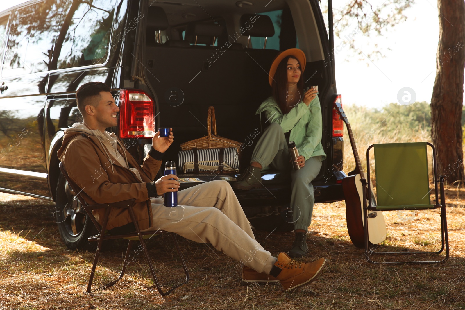 Photo of Couple resting near car and enjoying hot drink at camping site