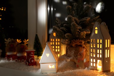 Christmas atmosphere. Beautiful glowing houses, fir trees, artificial snow and toys on window sill indoors