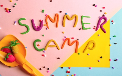 Photo of Flat lay composition with words SUMMER CAMP made from modelling clay, beads and plastic shovel on color background