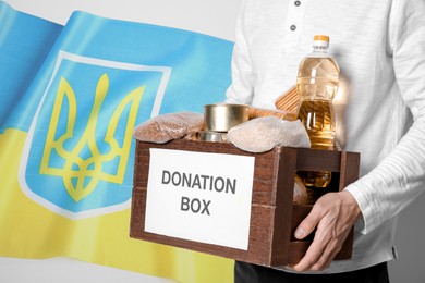 Image of Volunteer holding donation box with Ukrainian flag on background. Help during war