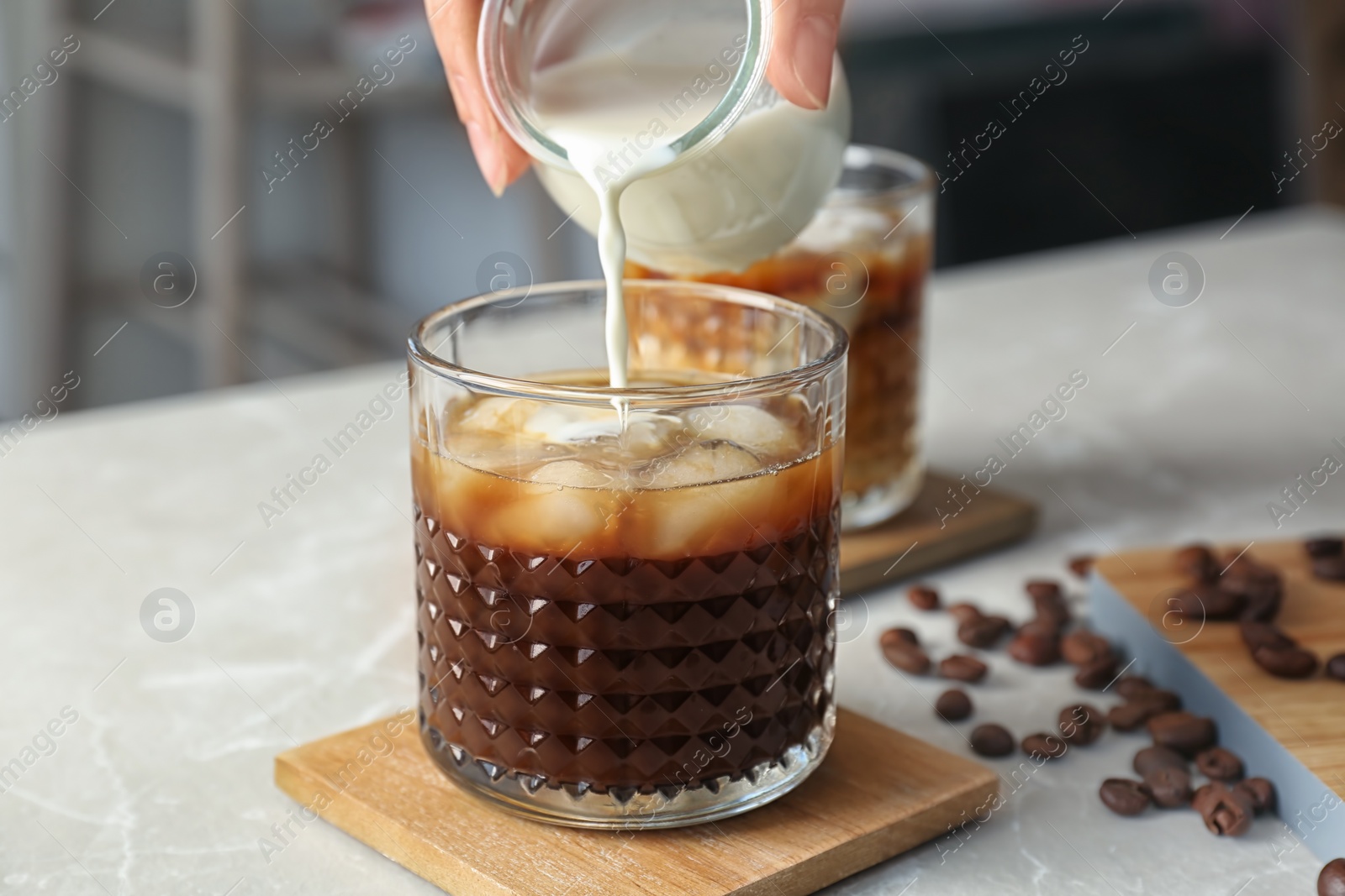 Photo of Woman pouring milk into glass with cold brew coffee on table