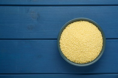 Bowl of raw couscous on blue wooden table, top view. Space for text
