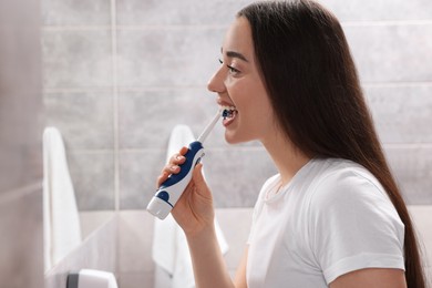 Photo of Young woman brushing her teeth with electric toothbrush near mirror in bathroom