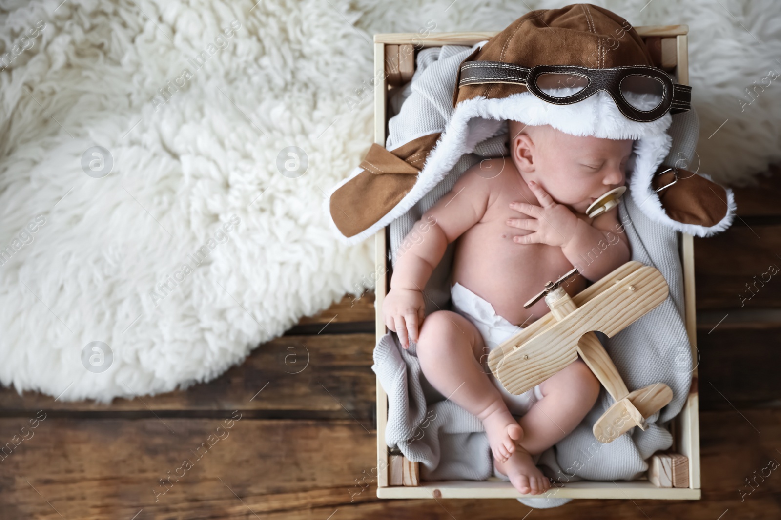 Photo of Cute newborn baby wearing aviator hat with toy sleeping in wooden crate, top view. Space for text