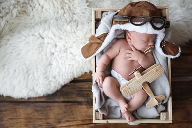 Photo of Cute newborn baby wearing aviator hat with toy sleeping in wooden crate, top view. Space for text