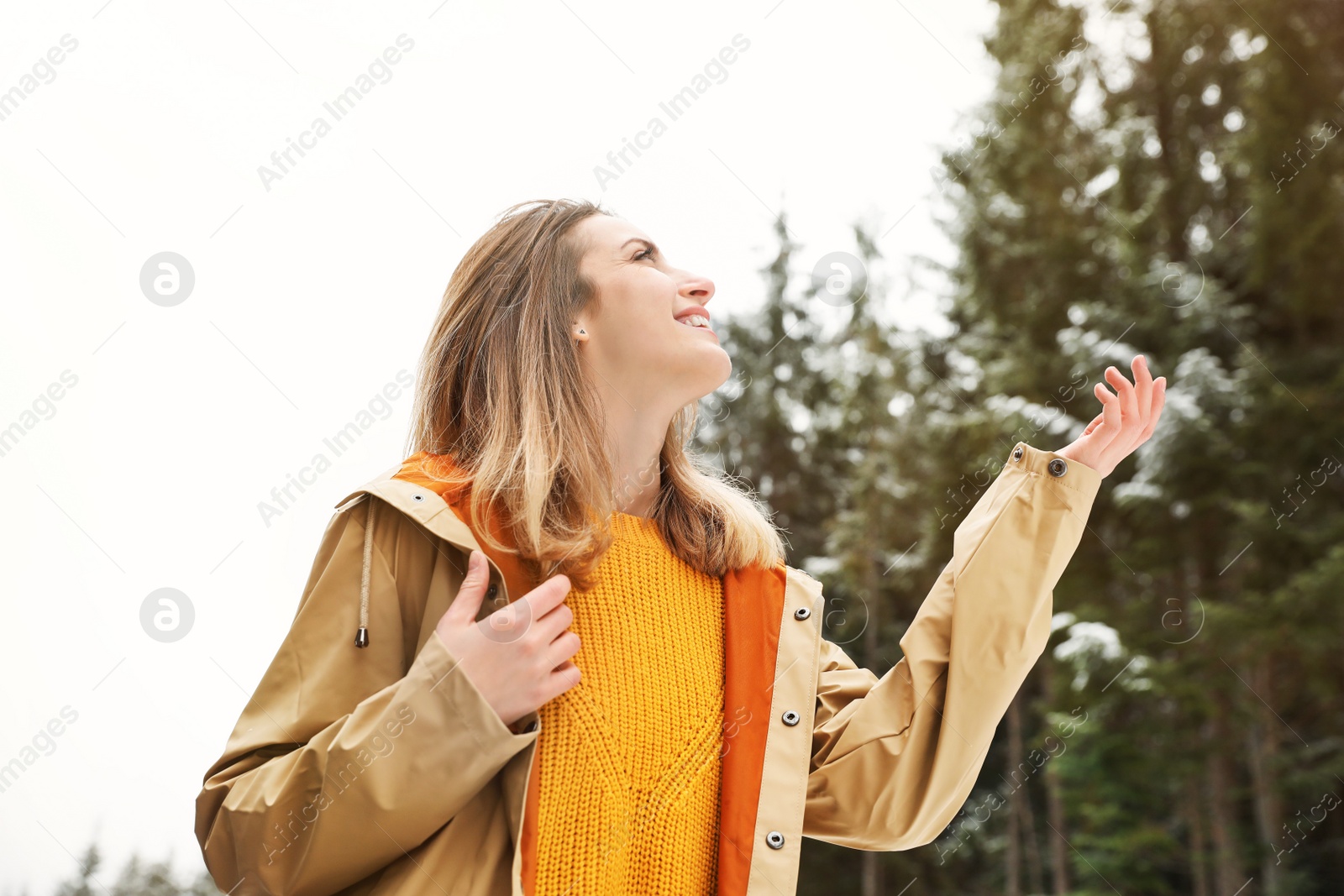Photo of Young woman in warm clothes catching snow outdoors. Winter vacation