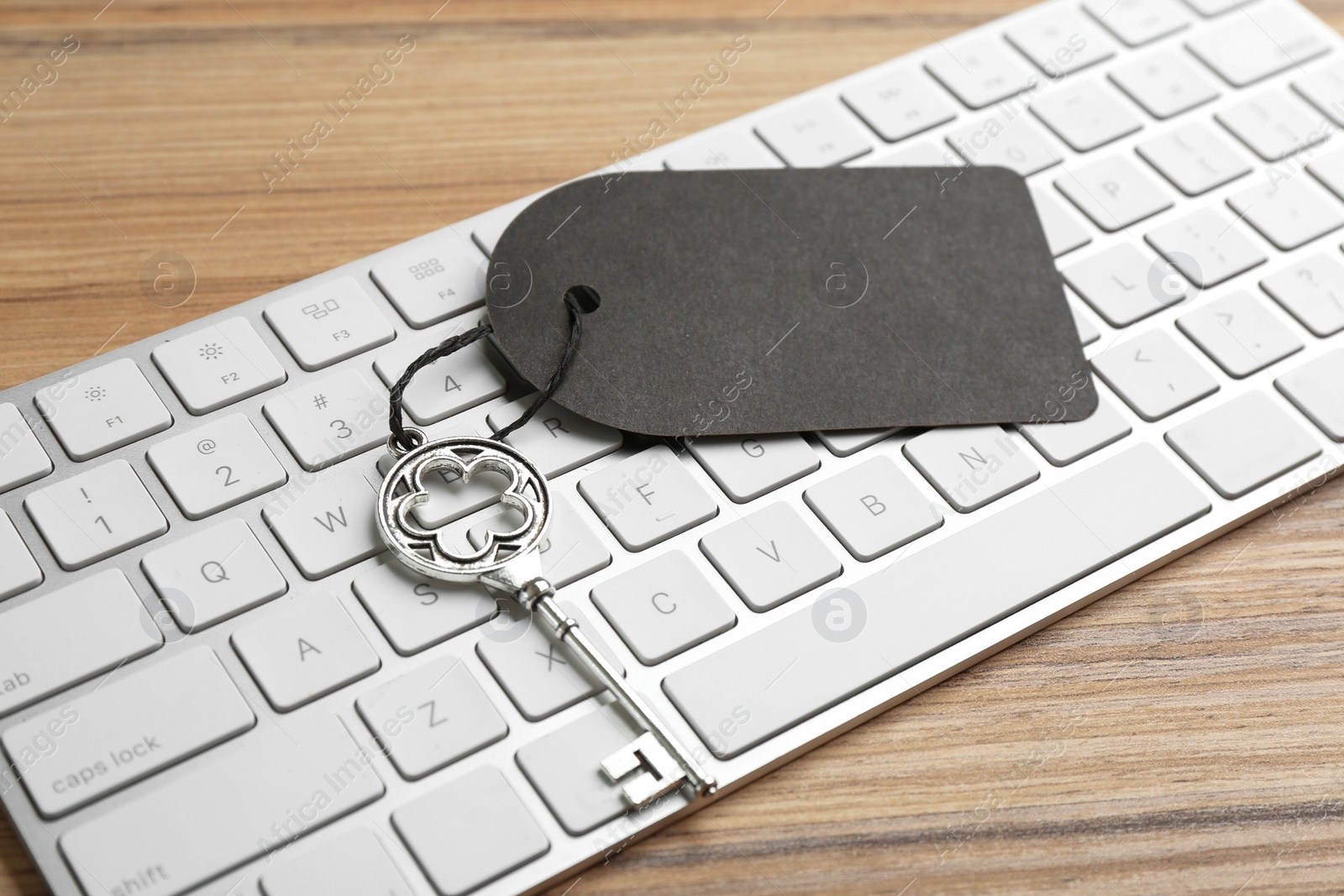 Photo of Vintage key with blank tag and keyboard on wooden table, closeup. Keyword concept