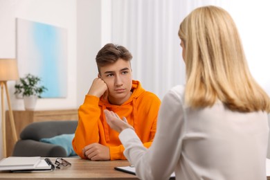 Psychologist working with teenage boy at table in office