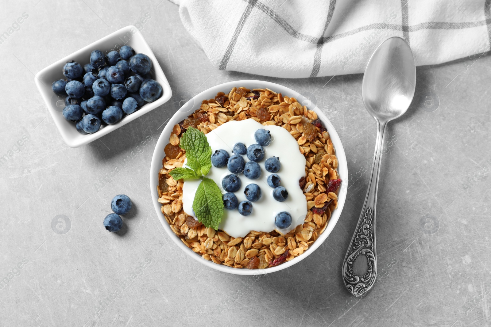 Photo of Delicious yogurt with granola and blueberries served on grey table, flat lay