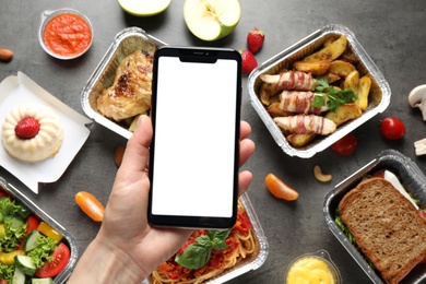 Photo of Top view of woman holding smartphone over grey table with lunchboxes, mockup for design. Healthy food delivery