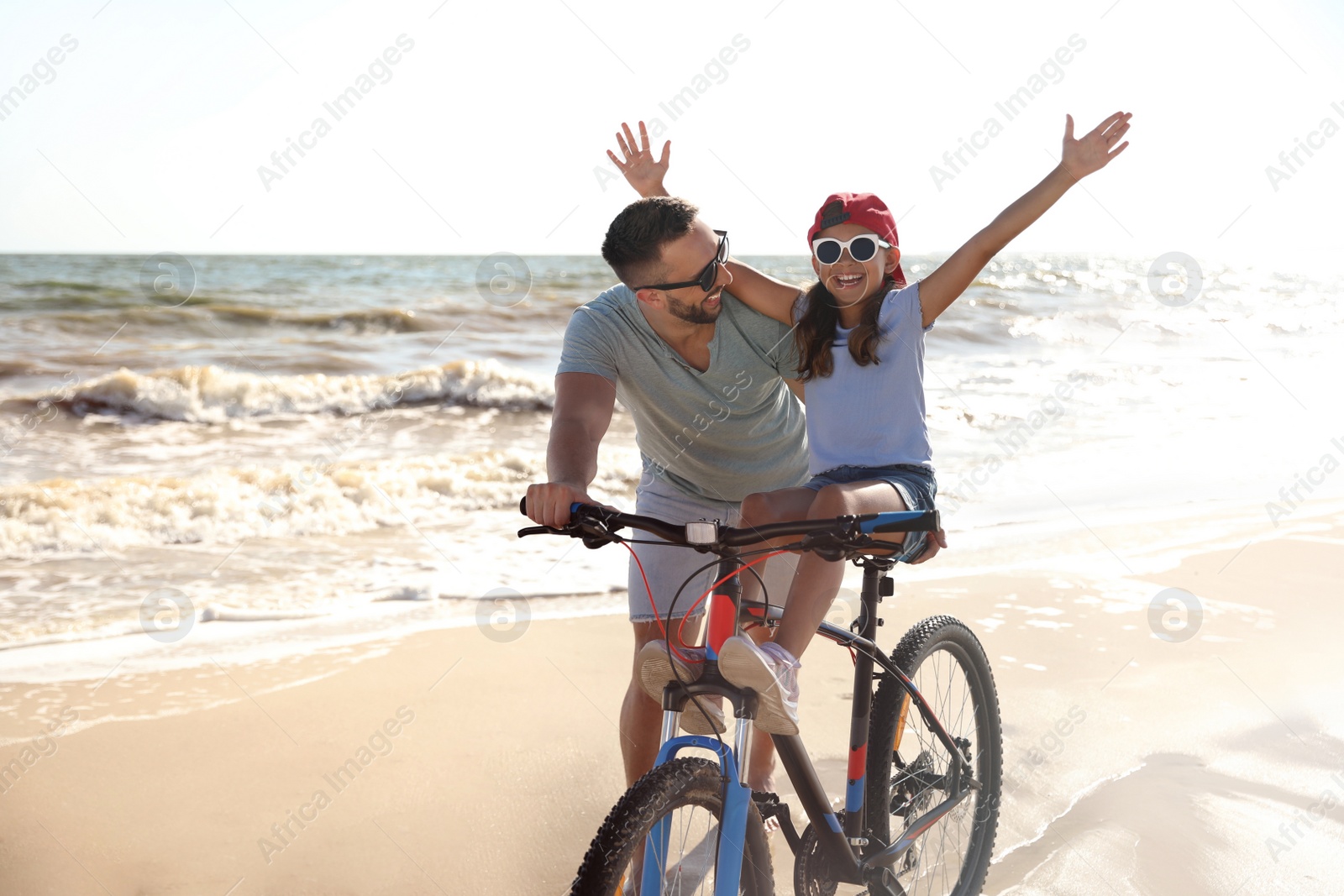 Photo of Happy father teaching daughter to ride bicycle on sandy beach near sea