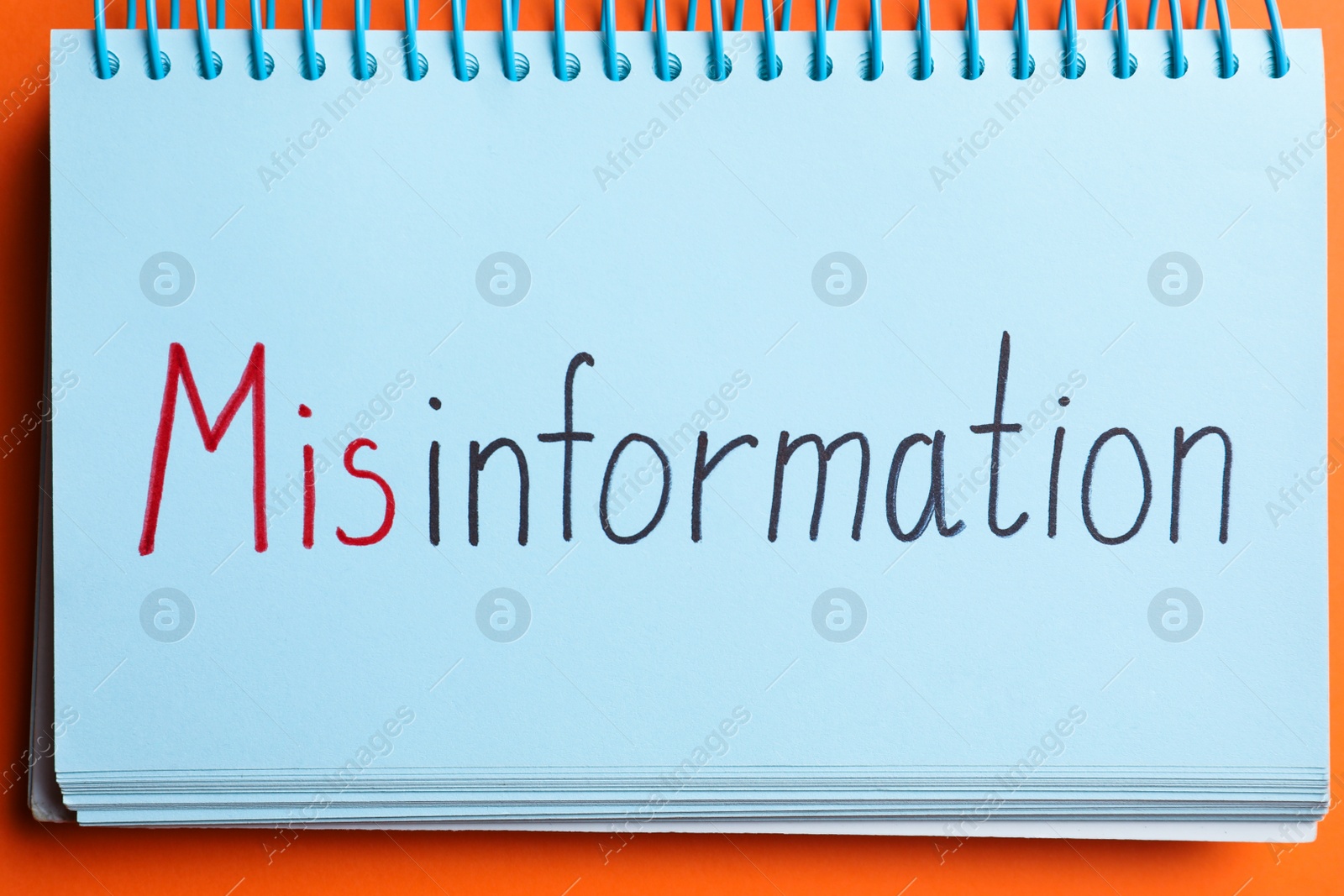 Photo of Notebook with word MISINFORMATION on orange background, top view