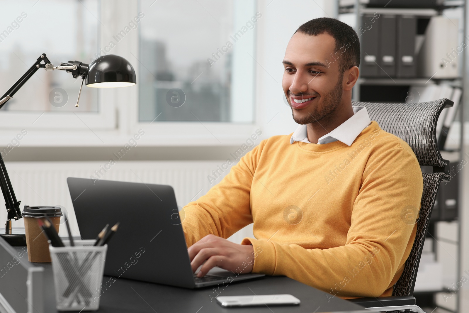 Photo of Young man working on laptop at table in office