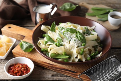 Photo of Delicious pasta with green peas, fresh basil and cheese on wooden table, closeup